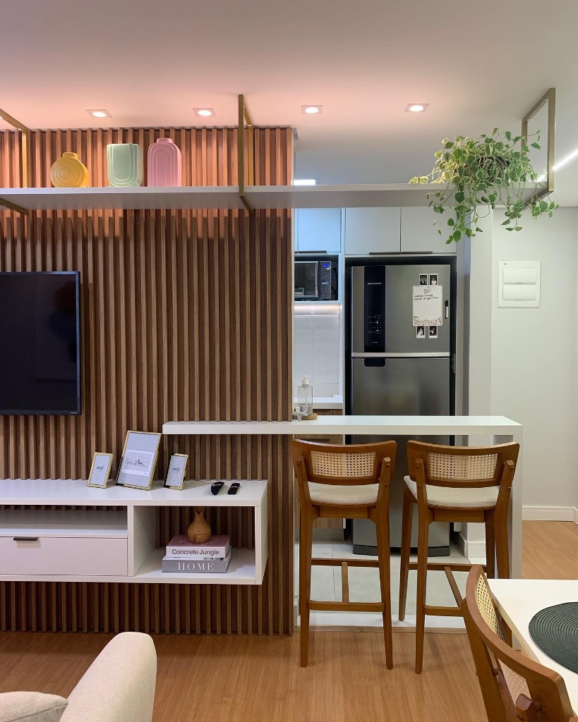 Cozinha integrada com sala de estar, painel ripado de madeira e banquetas.