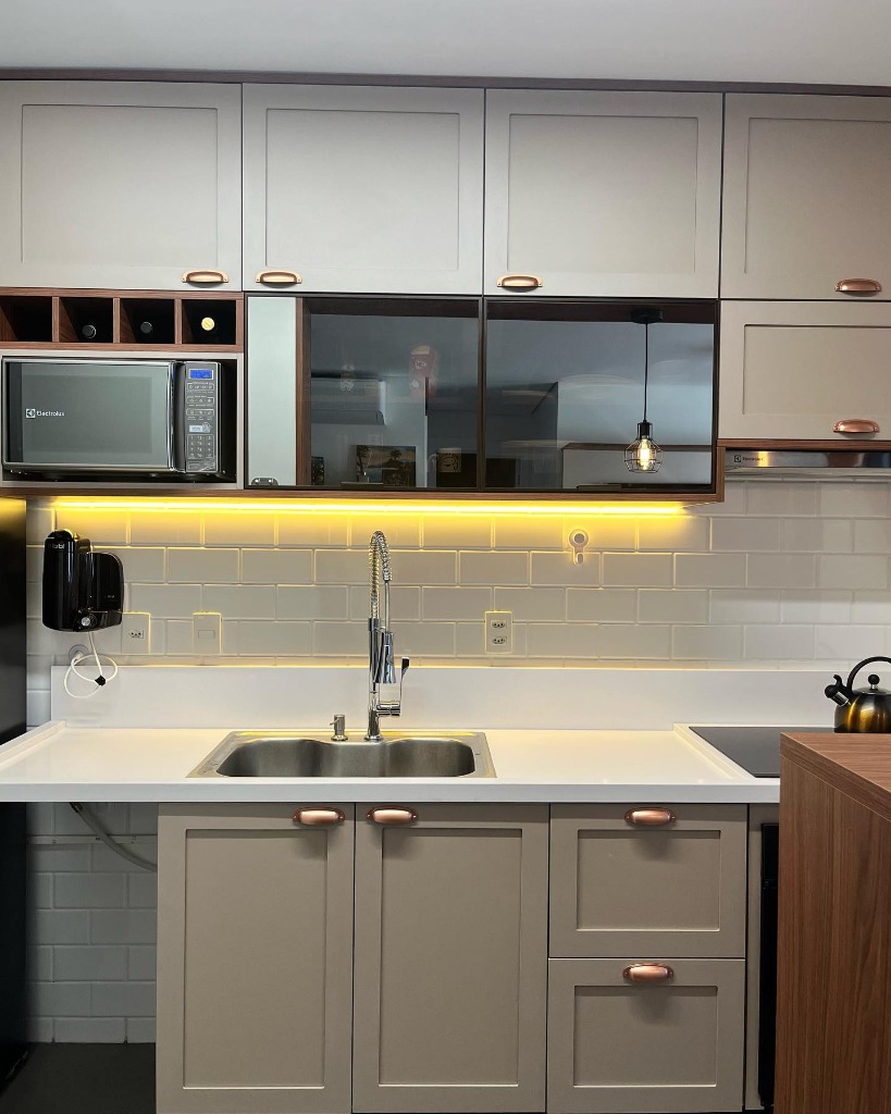 Cozinha planejada cinza com puxadores concha cobre e luzes LED.